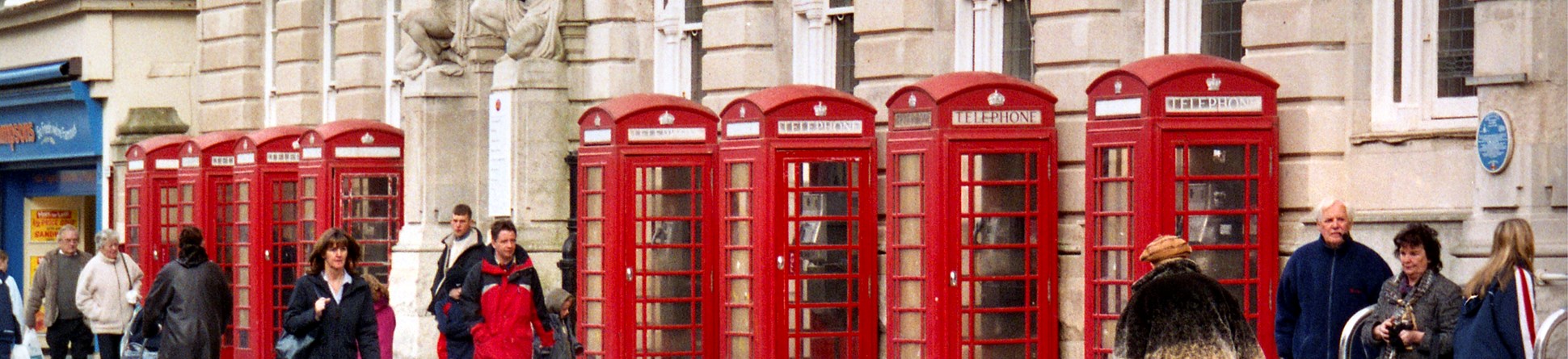 Group of eight K6 telephone kiosks with people walking past them