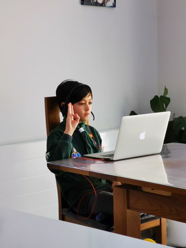 A young boy sits at a dining room chair and table dressed in a scouts uniform. He salutes a laptop.