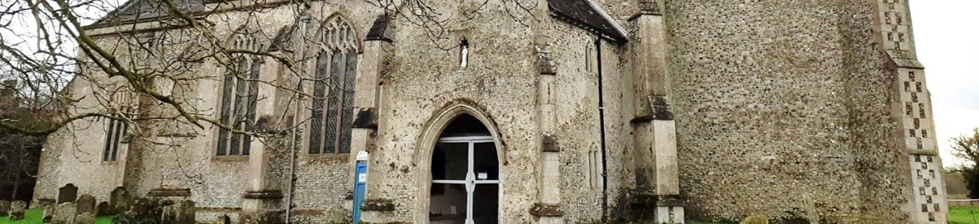 St Mary's Church North Tuddenham, a medieval stone church sitting in grassland with trees in the foreground.