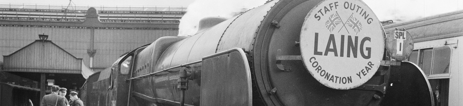 Steam train in station with a placard on the front which reads, 'LAING -  STAFF OUTING - CORONATION YEAR'