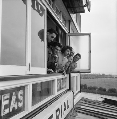 A group of men and a woman leaning out of a first floor window