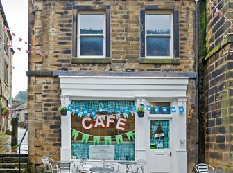 Rainy exterior of an urban cafe building with bunting and steel table sets outside. 