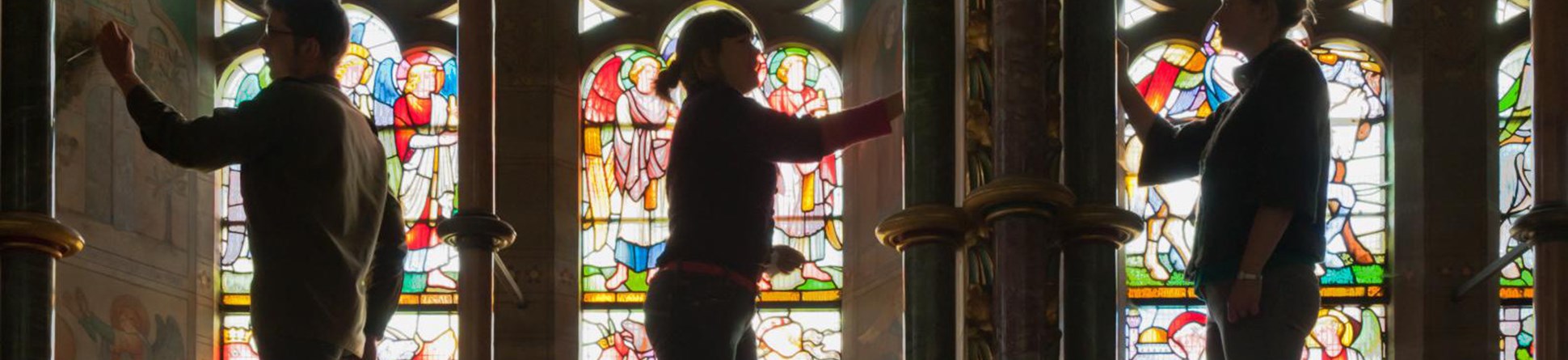 Photo of people silhouetted against stained glass windows