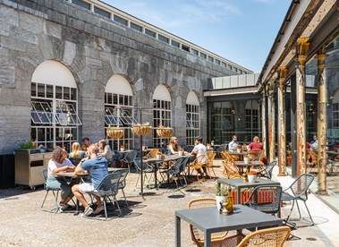 A photograph of people sat at tables in a restaurant's outdoor seating area.