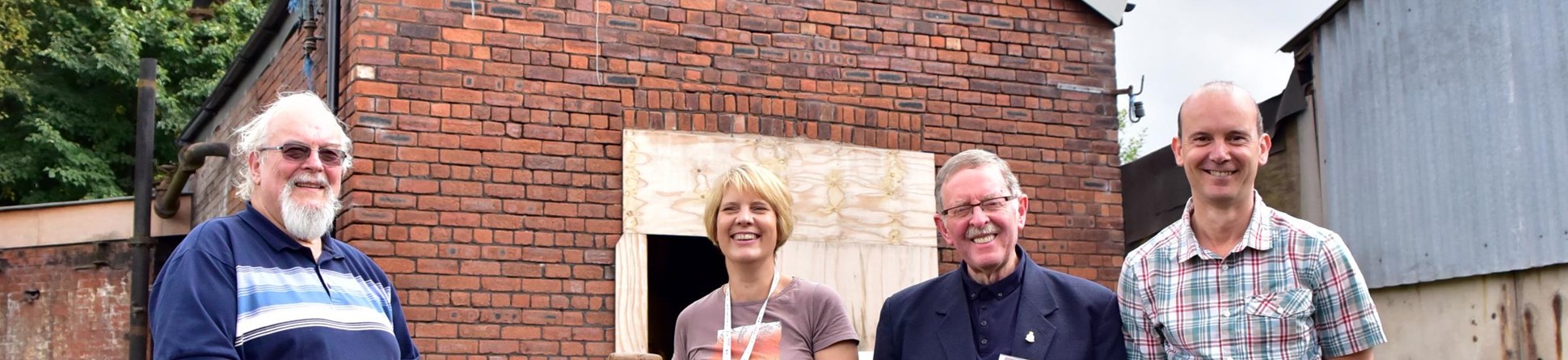 A group photo of four members of Middlewich Heritage Trust outside the brine pumps building at Murgatroyd's Brine Works.