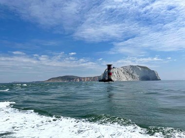 White water in the foreground, a lighthouse in front of a cliff in background 