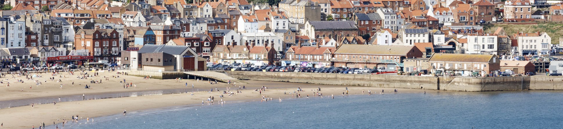 Daytime photo of the beach at Scarborough with a view of the gardens and castle above the bay. 