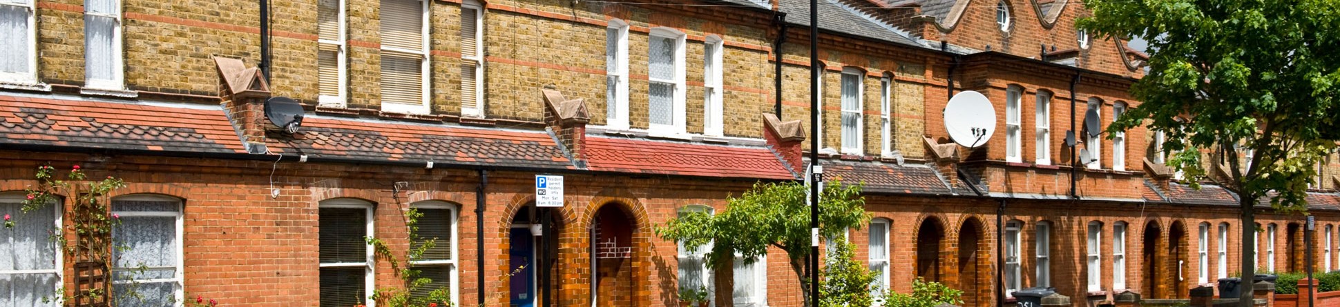 A row of red- and yellow-brick two-storey terraced houses, some with wheelie bins visible over the low wall bordering their front gardens.