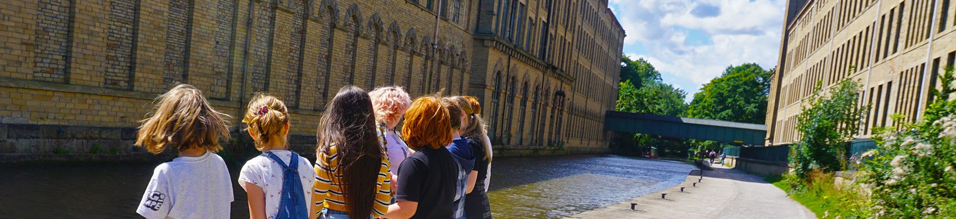 A group of children and one adult hold a rope on a canal towpath in an industrial landscape.