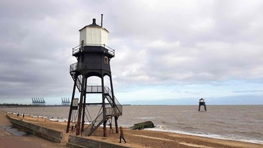 Iron framed lighthouse to the left and in the foreground with the sea in the background 