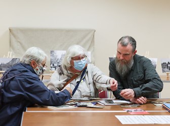 Photo of 2 women wearing face masks seated at a table looking at old photos with photographer Tony Mallon.