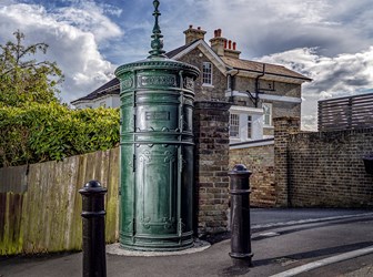 Late 19th-century cast iron cylindrical electricity substation with three rows of moulded cast iron patterned panels, projecting cornice, and foliated finial. 