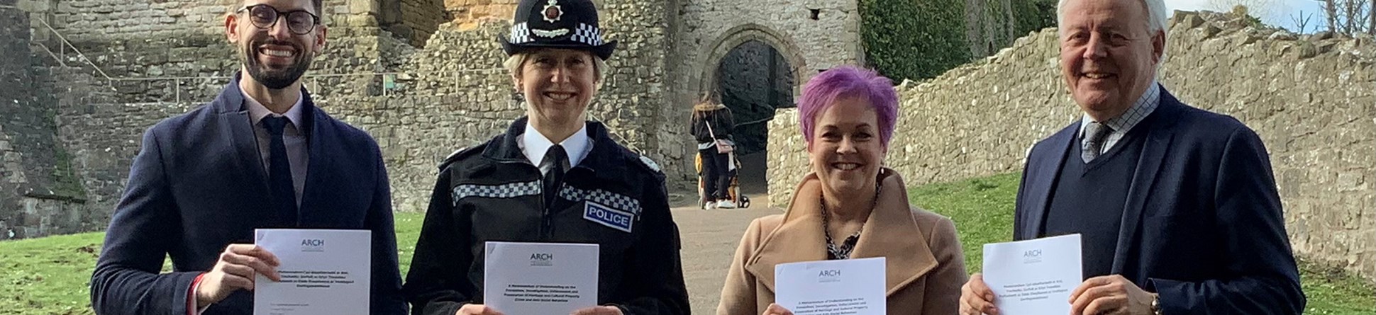 Four people each holding a document in front of castle ruins