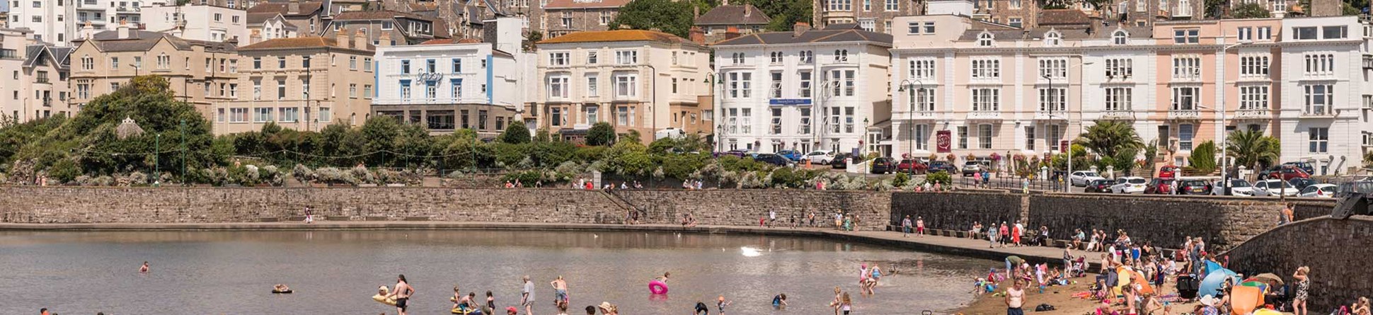 Busy beach with sea wall and Victorian terraces lining the seafront above the beach.