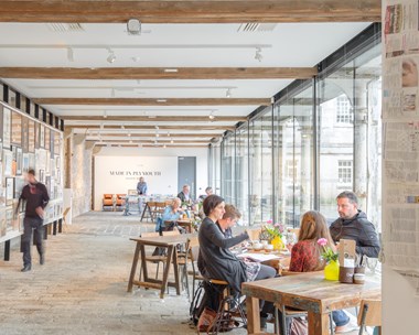 A photograph of a family sat at a wooden table in a light, airy café space with exposed wooden beams in the ceiling and flanked by glass panels to the side