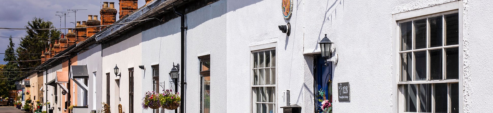 A row of one storey concrete cottages, in varying colours, with potted plants outside the front doors and window boxes.