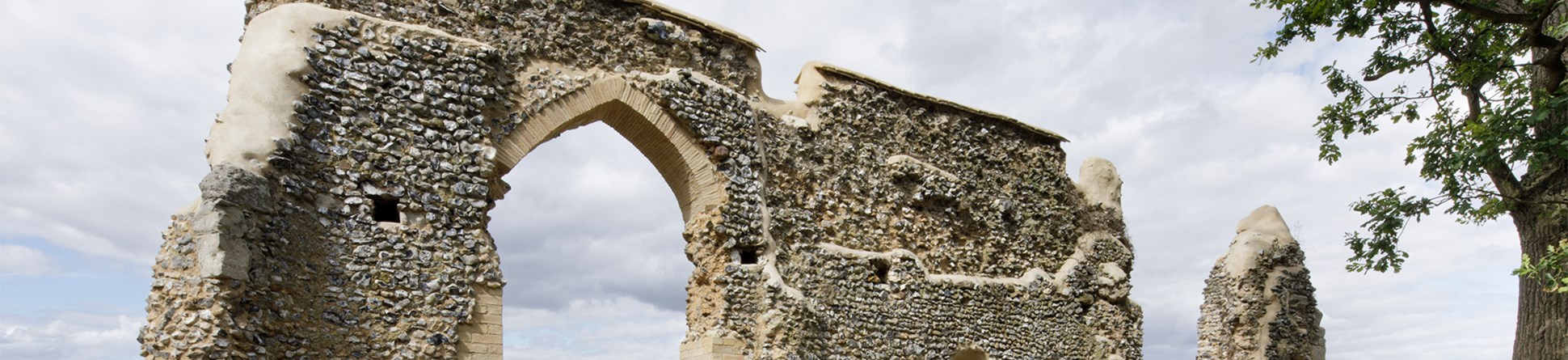 The ruined wall of the chapel shows an arched doorway and a flint-covered wall.