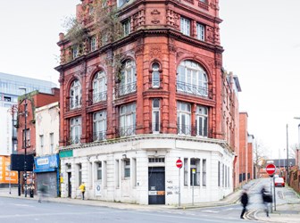 Exterior view of a building on a street corner with red upper floors and a white ground floor